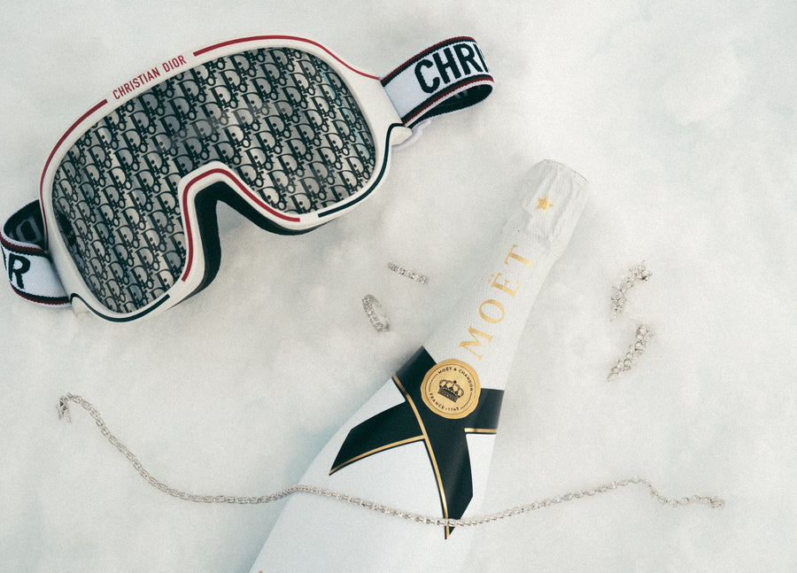 Designer ski goggles by Dior with champagne and diamond jewellery on the snow