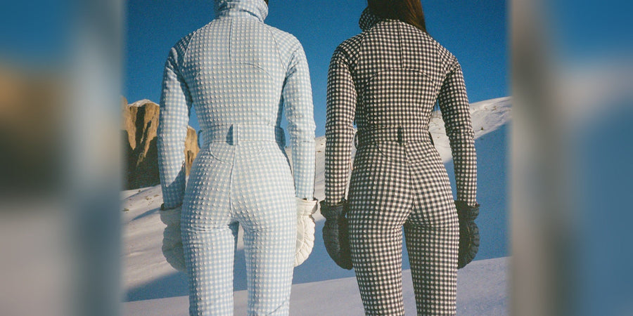 Two women in gingham one-piece ski suits on a sunny snowy slope